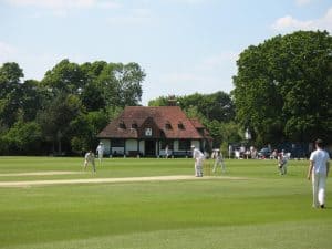 College sportsground showing the clubhouse and people playing cricket
