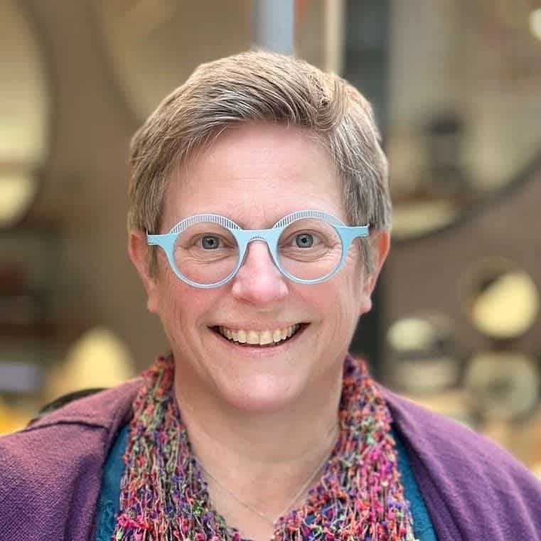 Portrait photograph of a smiling woman with light blue round glasses