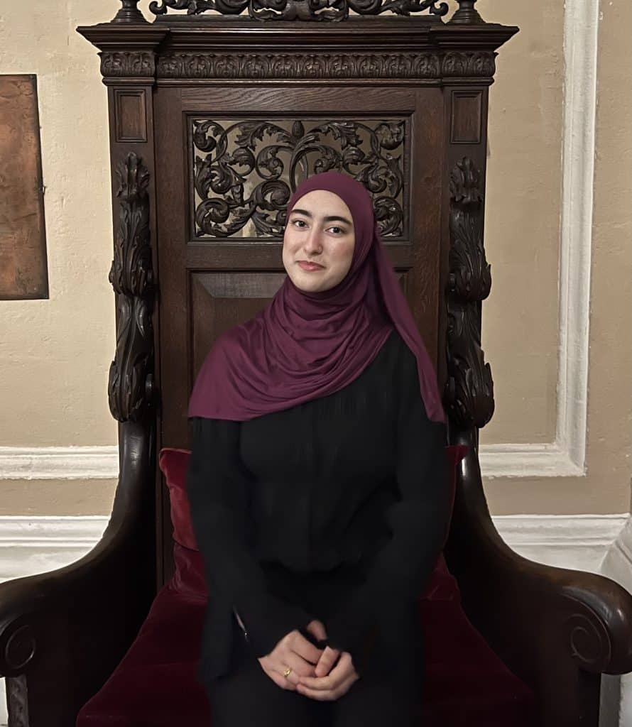 Mehreen profile photo: she is seated in a large ornately carved wooden chair